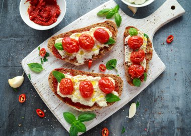 Domates Ricotta Bruschetta güneş ile kurutulmuş domates Yapıştır, zeytinyağı kahverengi ekmek ve Beyaz ahşap tahta fesleğen.
