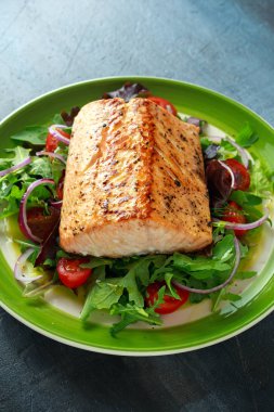 Domates, soğan, yeşil karışımı ile pişmiş somon steak salata bir tabak içinde bırakır. sağlıklı gıda