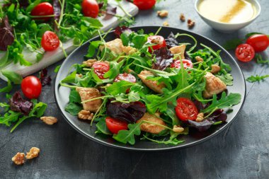 Taze salata tavuk göğsü, roka, fındık ve ahşap bir masa içinde siyah plaka üzerinde domates ile.