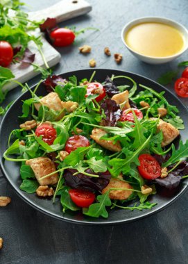 Taze salata tavuk göğsü, roka, fındık ve ahşap bir masa içinde siyah plaka üzerinde domates ile.