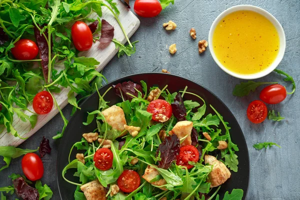 Taze salata tavuk göğsü, roka, fındık ve ahşap bir masa içinde siyah plaka üzerinde domates ile.