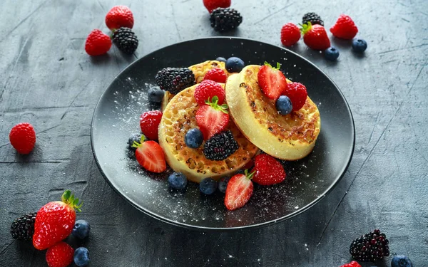 British Crumpets breakfast with blueberries, strawberries, blackberries, raspberries drizzled with icing sugar — Stock Photo, Image