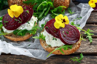 Rustik kepekli çörek süzme peynir ile roket bırakır, pancar dilimleri ve yenilebilir viola çiçekler. Vejetaryen yiyecekler snack.