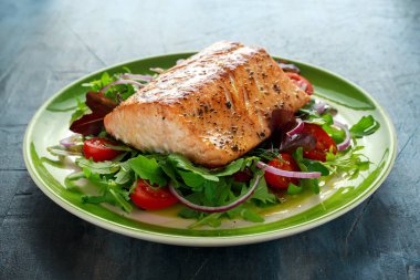 Domates, soğan, yeşil karışımı ile pişmiş somon steak salata bir tabak içinde bırakır. sağlıklı gıda
