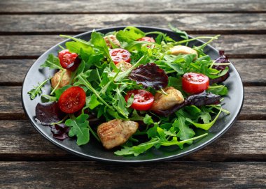 Taze salata tavuk göğsü, roka, fındık ve ahşap bir masa içinde siyah plaka üzerinde domates ile.