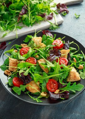 Taze salata tavuk göğsü, roka, fındık ve ahşap bir masa içinde siyah plaka üzerinde domates ile.