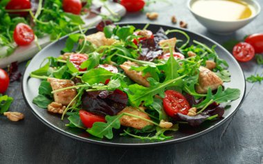 Taze salata tavuk göğsü, roka, fındık ve ahşap bir masa içinde siyah plaka üzerinde domates ile.