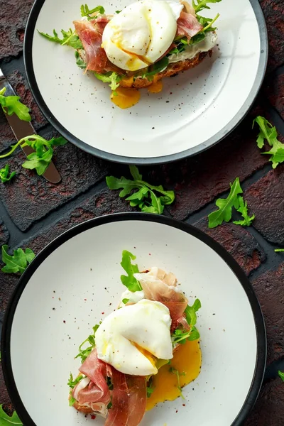 Bruschetta com creme de queijo, rúcula selvagem, presunto de parma e ovo escalfado servido em prato branco . — Fotografia de Stock