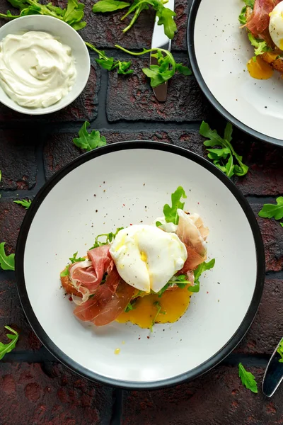 Bruschetta com creme de queijo, rúcula selvagem, presunto de parma e ovo escalfado servido em prato branco . — Fotografia de Stock