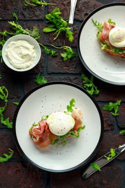 Beyaz tabakta Bruschetta krem peynir, wilde rucola, parma jambonu ve haşlanmış yumurta.