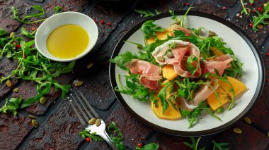 Taze roka, parma jambonu, zeytin yağı, kabak çekirdeği ve otlar ile lezzetli Trabzon hurması salata. Sonbahar, kış sağlıklı gıda