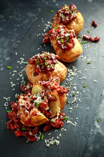 Baked jacket potatoes topped with red kedney beans in tomato sauce and chives served on stone board