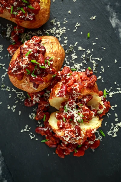 Baked jacket potatoes topped with red kedney beans in tomato sauce and chives served on stone board