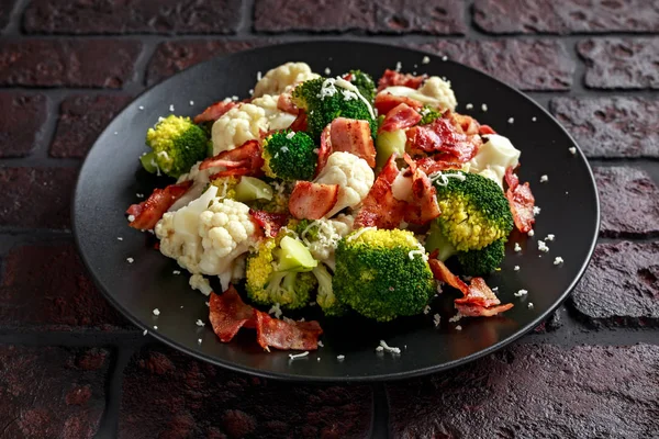 Broccoli al vapore, insalata di cavolfiore con pancetta, parmigiano in un piatto nero. concetto di cibo sano — Foto Stock