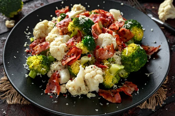 Broccoli al vapore, insalata di cavolfiore con pancetta, parmigiano in un piatto nero. concetto di cibo sano — Foto Stock