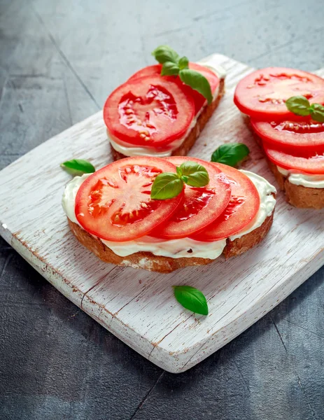 Bruschetta, toast med mjuk ost, basilika och tomater på en vit träplatta. Italienska hälsosamt mellanmål, mat. — Stockfoto