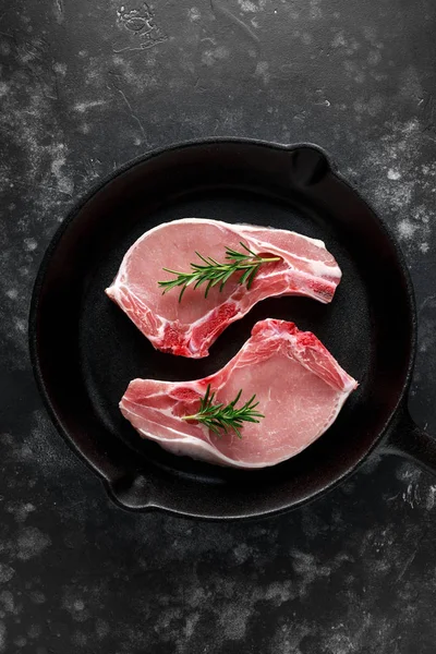 Сырая свиная лоза отбивные в деревенском сковороде, сковорода с розмарином. вид сверху. фон — стоковое фото