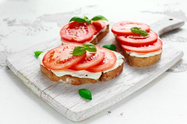 Bruschetta, kızarmış peynir, fesleğen ve Beyaz ahşap tahta üzerinde domates ekmek. İtalyan sağlıklı snack, gıda.