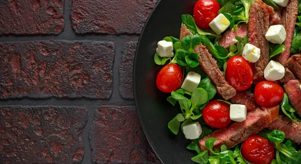 수 분이 많은 쇠고기 등심 스테이크 샐러드와 구운된 토마토, feta 치즈와 검정 잉크 판에 녹색 야채. 건강에 좋은 음식 — 스톡 사진