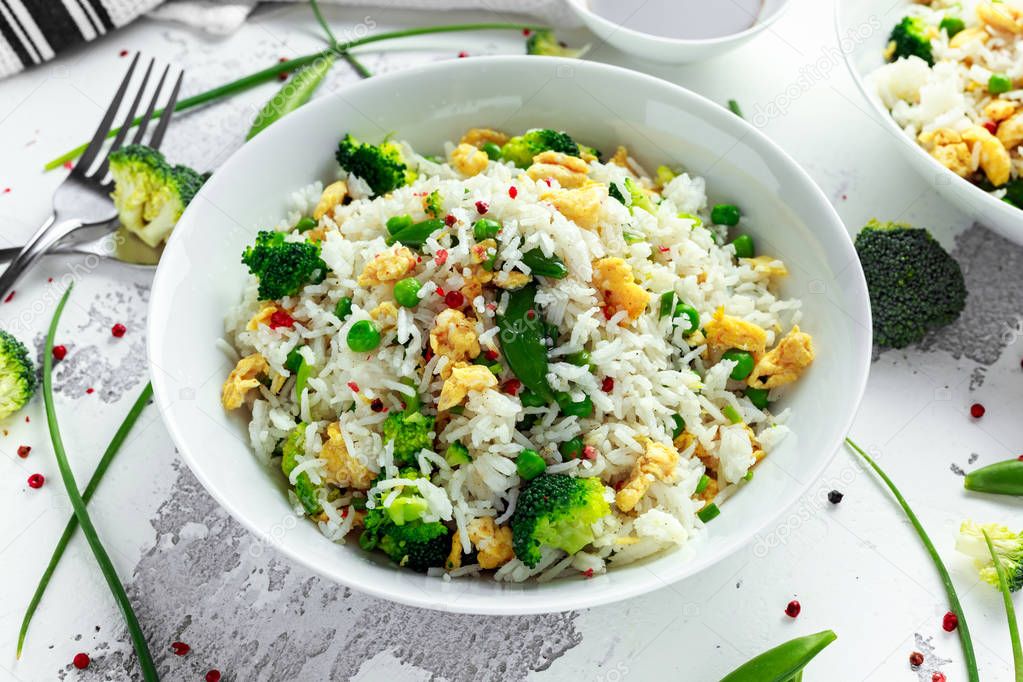 Fried rice with vegetables, broccoli, peas and eggs in a white bowl. soy sauce. healthy food