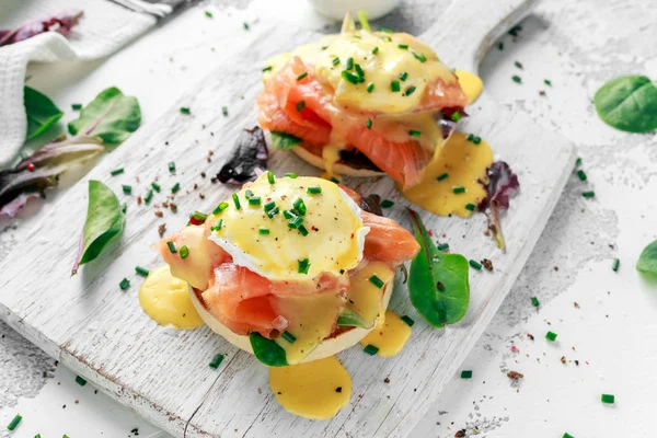 Ovos Benedict em muffin inglês com salmão defumado, mistura de salada de alface e molho holandês na placa branca — Fotografia de Stock