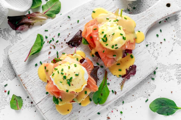 Yumurta Benedict İngiliz çöreği somon füme, marul salata karışımı ve hollandaise soslu beyaz tahta üzerinde üzerinde — Stok fotoğraf