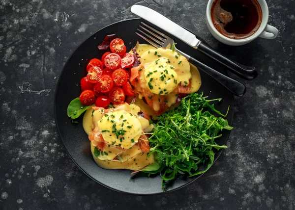 Ovos Benedict em muffin inglês com salmão defumado, foguete selvagem e molho holandês em um prato preto . — Fotografia de Stock