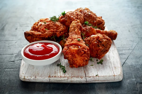 Fried crispy chicken legs, Thigh on white cutting board with ketchup and herbs