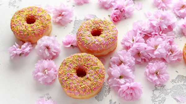 Свежий розовый пончик украшен цветком вишневого дерева — стоковое фото