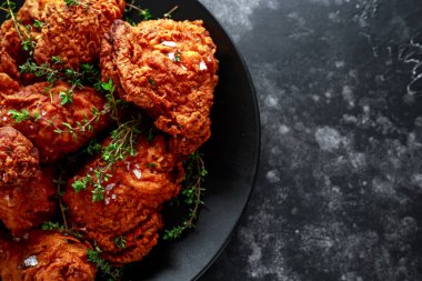 Kızarmış gevrek tavuk budu, uyluk otlar ile siyah bir tabak içinde.