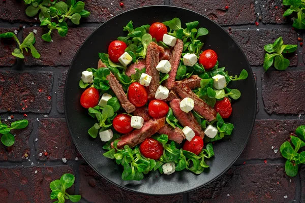 Juicy Beef Sirloin Steak Salad with roasted tomatoes, feta cheese and green vegetables in a black plate. healthy food — Stock Photo, Image