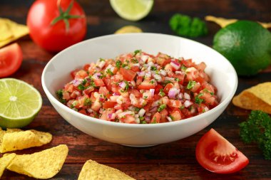 Limon, kırmızı soğan, jalapeno biber, maydanoz ve ahşap masada tortilla cips ile beyaz kapta Meksika Domates Salsa
