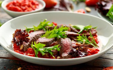 Romesco soslu biftek, beyaz tabakta fındık ve sebze.