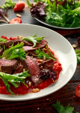 Romesco soslu biftek, beyaz tabakta fındık ve sebze.