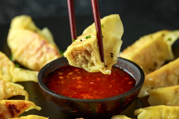 Bacchette che tengono e immergono gnocchi di carne, gyoza yaki fritti in salsa di peperoncino dolce . — Foto Stock