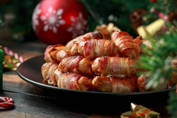 Christmas Pigs in blankets, sausages wrapped in bacon with decoration, gifts, green tree branch on wooden rustic table — Stock Photo, Image