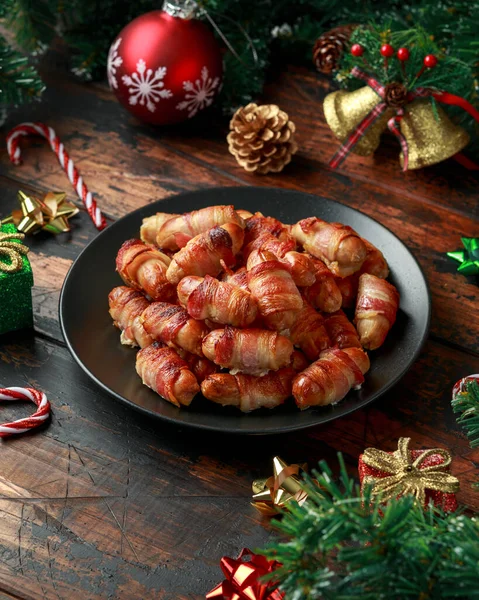 Christmas Pigs in blankets, sausages wrapped in bacon with decoration, gifts, green tree branch on wooden rustic table — Stock Photo, Image