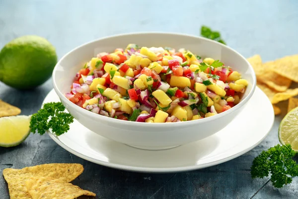 Bowl of fresh Mango Salsa with nachos chips and herbs. Healthy Vegan, Vegetables food.