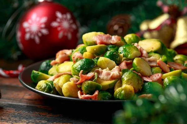 Cavoletti di Bruxelles natalizi e pancetta con decorazione, regali, ramo d'albero verde su tavola rustica in legno — Foto Stock