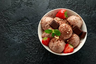 Koyu çikolatalı dondurma, beyaz kasede çilek ve fındık.
