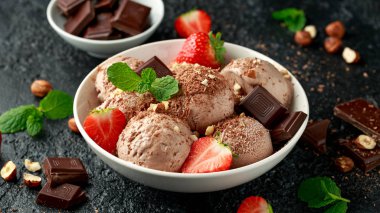 Koyu çikolatalı dondurma, beyaz kasede çilek ve fındık.
