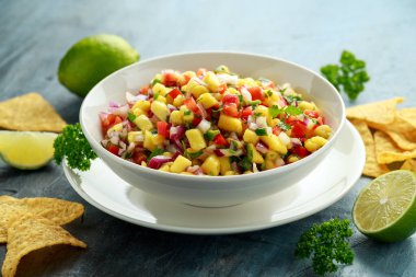 Bir kase taze mango salsa, yanında cips ve ot. Sağlıklı vejetaryen, sebze.