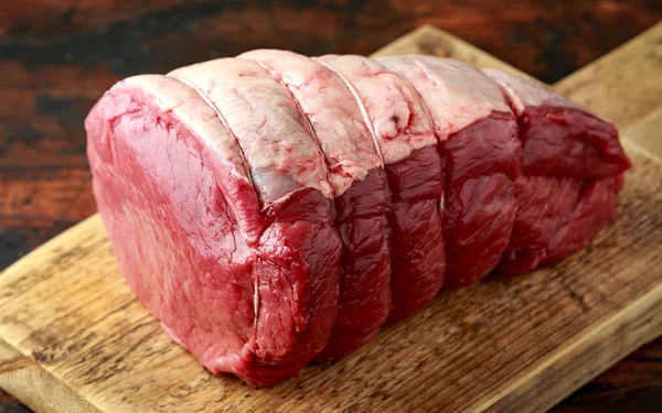 Butcher slicing Fresh Raw top side beef meat on rustic wooden chopping board — Stock Photo, Image