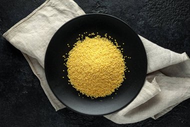 Millet tahıl taneleri siyah tabağa dökülüyor. Organik konsept