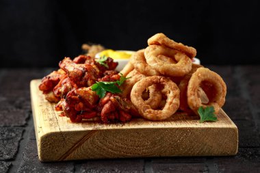 Yapış yapış tavuk kanatları ve limon, ketçap ve hardalla servis edilen yağda kızartılmış soğan halkaları. Yağlı, fast food konsepti