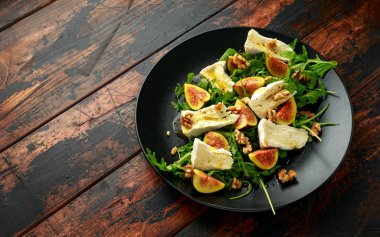 Vejetaryen peyniri, incir ve Arugula. Siyah tabakta servis edilen sıcak roket salatası.