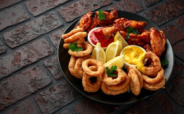 Yapış yapış tavuk kanatları ve limon, ketçap ve hardalla servis edilen yağda kızartılmış soğan halkaları. Yağlı, fast food konsepti