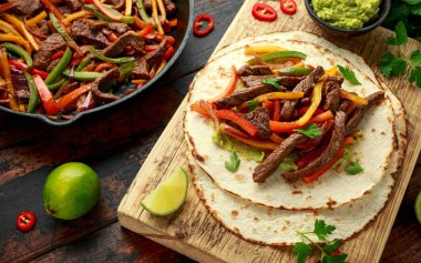 Biber, soğan ve ahşap tahtada avokado karışımlı biftek Fajitas.