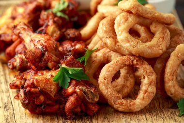 Yapış yapış tavuk kanatları ve limon, ketçap ve hardalla servis edilen yağda kızartılmış soğan halkaları. Yağlı, fast food konsepti