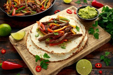 Biber, soğan ve ahşap tahtada avokado karışımlı biftek Fajitas.